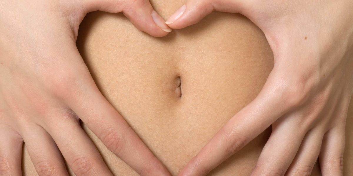 A woman's hands forming a heart symbol around navel
